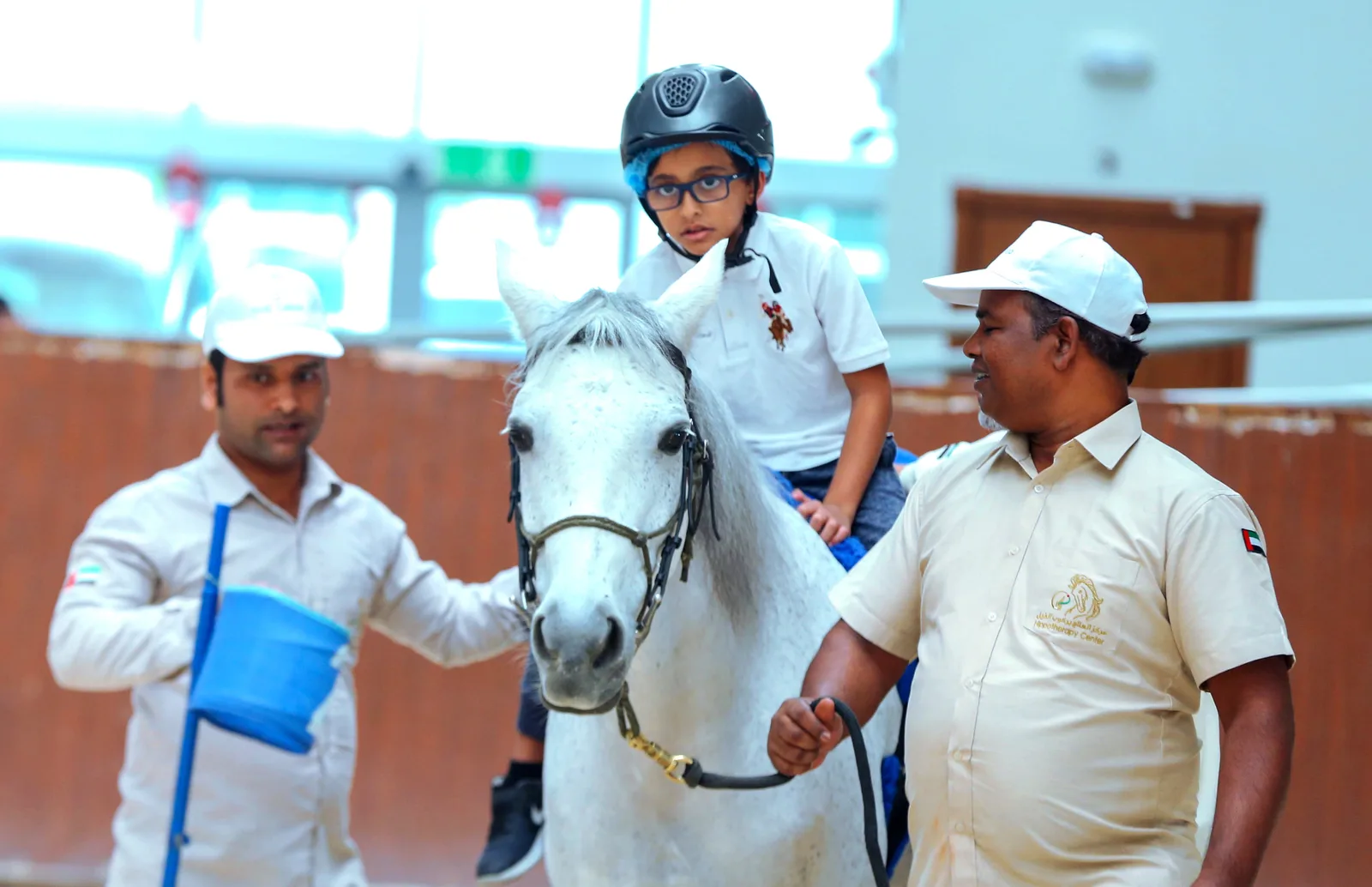 A child wearing a helmet on a horse with two adults alongside